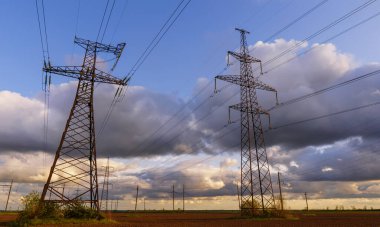 Güzel bulutlu bir gökyüzünün arka planında tarladan geçen yüksek voltajlı elektrik hatları..