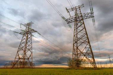 Güzel bulutlu bir gökyüzünün arka planında yeşil bir alandan geçen yüksek voltajlı elektrik hatları..