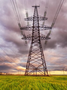 Güzel bulutlu bir gökyüzünün arka planında yeşil bir alandan geçen yüksek voltajlı elektrik hatları..