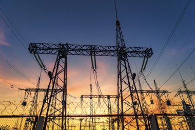 Yüksek voltajlı elektrik hatlarının silueti gün doğumunda ya da günbatımında renkli bir gökyüzüne karşı.