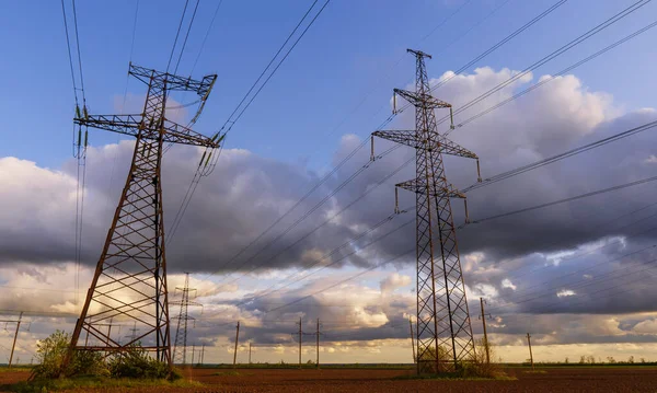 Güzel bulutlu bir gökyüzünün arka planında tarladan geçen yüksek voltajlı elektrik hatları..