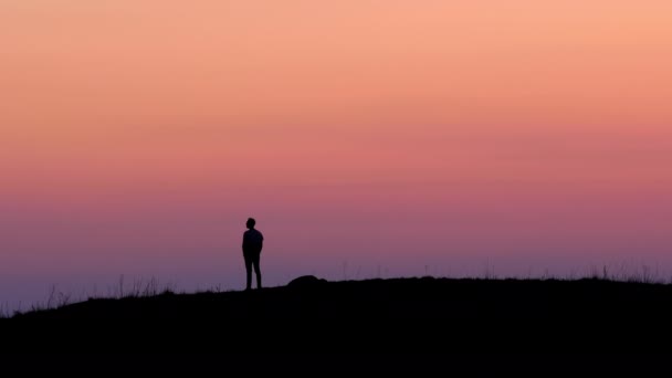 Silueta de un hombre de pie en la cima de una colina contra un cielo ardiente al atardecer - logro de la libertad - 4k — Vídeos de Stock