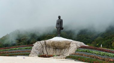 Güzel bir heykel, sisle kaplanmış kayalık bir çıkıntıya yükselir ve canlı renkli çiçeklerle çerçevelenir Chiang Mai. 