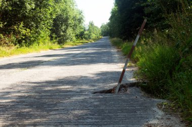 Kırsal kesimde yol kenarlarında çukurlar ve çukurlar olan tehlikeli beton bir yol. Yolda bir çukur uyarı kolonu ile işaretlenmiş..