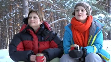 Kış, bir piknik, çay içme ve gülüyor, ateşin yanında oturan iki kadın
