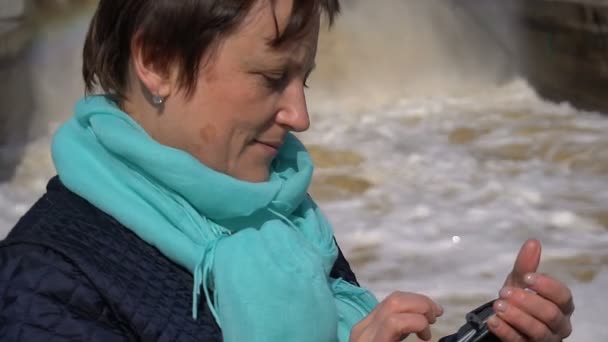 Mujer viendo una foto en su teléfono en el fondo de la cascada del arco iris. Día soleado . — Vídeo de stock