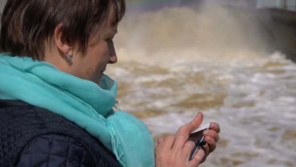 Frau beim Betrachten eines Fotos auf Ihrem Handy vor dem Hintergrund des Regenbogenwasserfalls. sonniger Tag. — Stockvideo