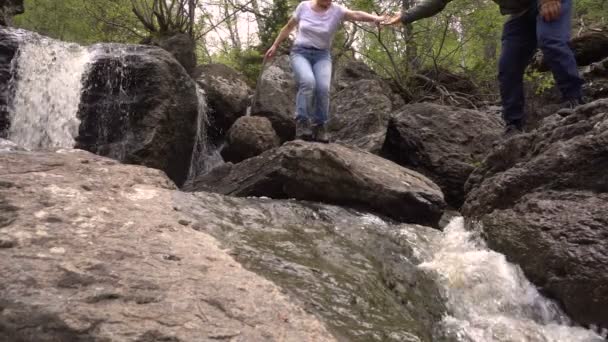Egy pár férfi és női turisták ugrás hegyi folyó vízesés a háttérben nyári nap — Stock videók