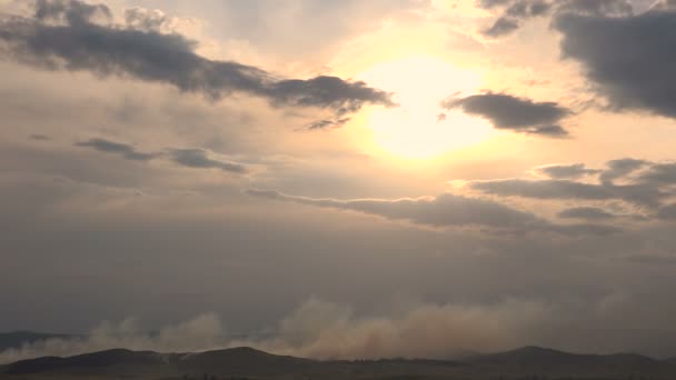 Fuego en un bosque de montaña al atardecer. El humo sube por encima de las laderas de las montañas — Vídeos de Stock