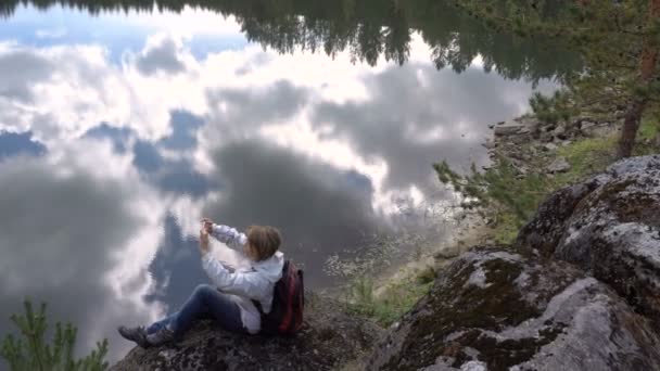 Kvinna turist i bakgrunden reflektion av moln i sjön fotograferade Smartphone landskapet. — Stockvideo