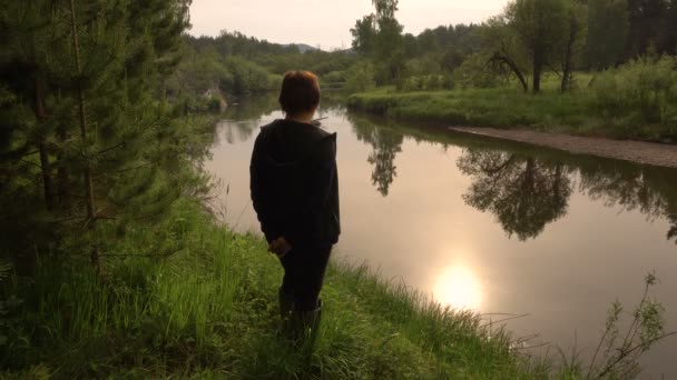 Mujer silueta en la orilla del río en la madrugada. Reflexión del Sol en el Deseo — Vídeos de Stock