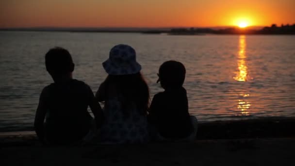 Gutter og jenter ser på solnedgangen over havet – stockvideo