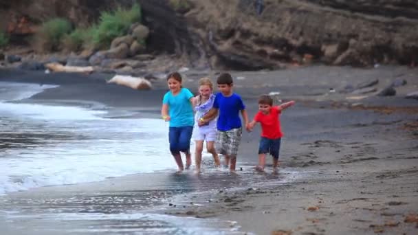 Дети бегают по пляжу вдоль линии серфинга — стоковое видео