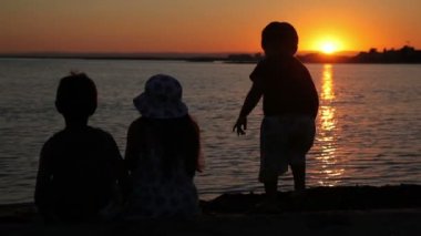 Çocuklar denizin üzerinde gün batımını izliyor