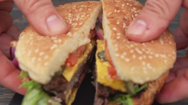 Mannelijke handen openen verse zelfgemaakte gegrilde hamburger gesneden in twee helften — Stockvideo