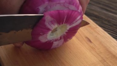 Bıçağın yakın plan çekimi ahşap tahtanın üzerindeki halkalara mor soğanı kesiyor.