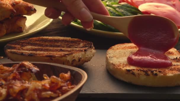 Primer plano de las manos extendiendo una salsa de tomate en el bollo en la hamburguesa a la parrilla — Vídeo de stock
