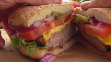 Erkek ellerinin iki parçaya bölünmüş ev yapımı ızgara burgeri açtığı yakın plan.