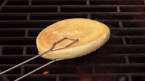 Close-up van hamburgerbroodje geplaatst op het grillrooster met keukentangen — Stockvideo