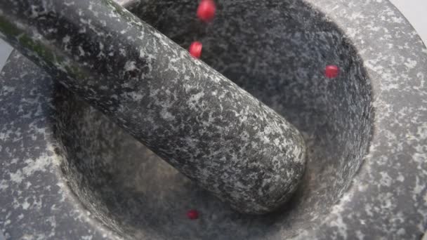 Primer plano de granos de pimienta rosa picante cayendo en el mortero de piedra gris — Vídeos de Stock
