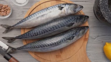 Ellerin üst görüntüsü yuvarlak ahşap tahtaya üç uskumru balığı koyuyor.