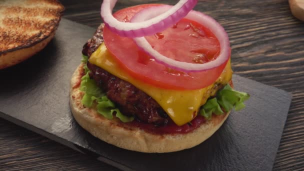 Anillos de cebolla se colocan en la parte superior de la hamburguesa a la parrilla casera fresca — Vídeo de stock