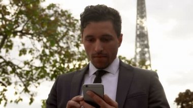 Siyah takım elbiseli genç ve çekici iş adamı cep telefonuyla yazı yazıyor.