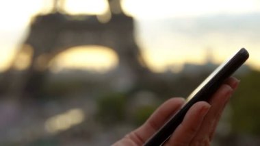 Eyfel Kulesi 'nin arka planındaki telefon ekranına kadın eli tıklıyor.