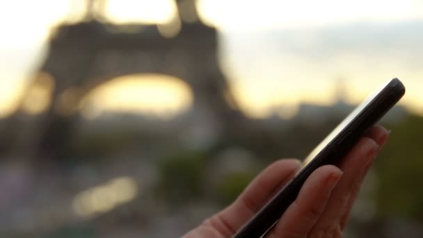 La mano femenina hace clic en la pantalla del teléfono en el fondo de la Torre Eiffel — Vídeo de stock