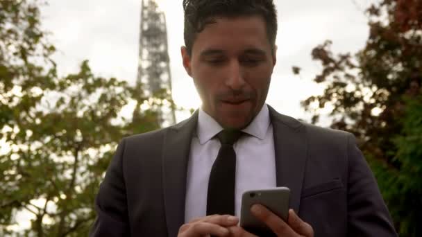 En ung affärsman i svart kostym tittar på sin mobil och ler — Stockvideo