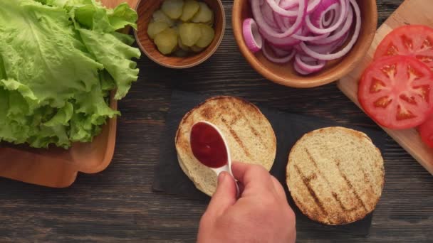 Bovenaanzicht van tomatensaus die zich verspreidt over het zelfgemaakte gegrilde hamburgerbroodje — Stockvideo