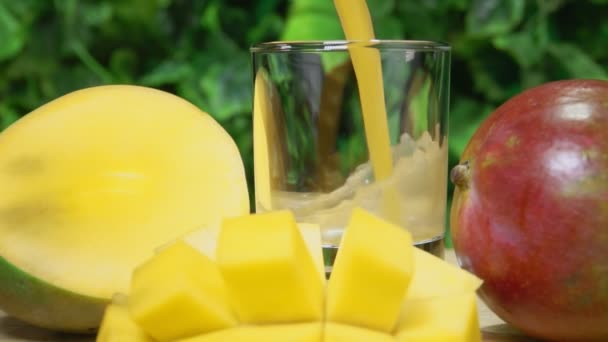 Сок манго наливают в стакан рядом с большим спелым манго, разрезанным на ломтики — стоковое видео