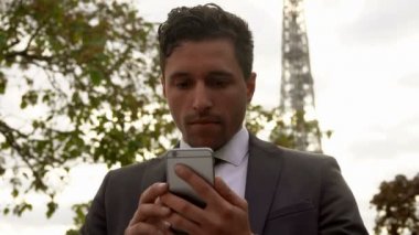 İş adamı Eyfel Kulesi 'nin arka planında cep telefonuna ciddi ciddi bakıyor.