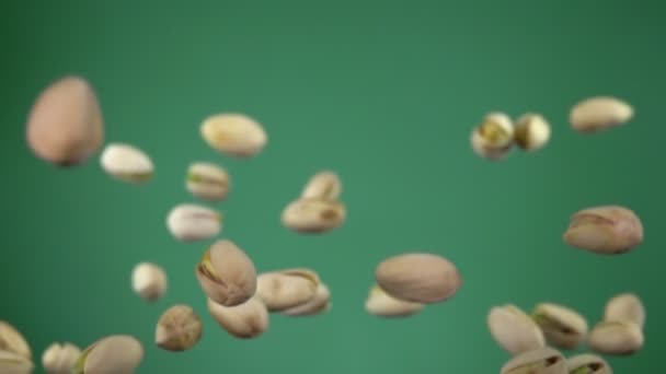 Närbild av läckra saltade pistaschmandlar flyger upp på en grön bakgrund — Stockvideo