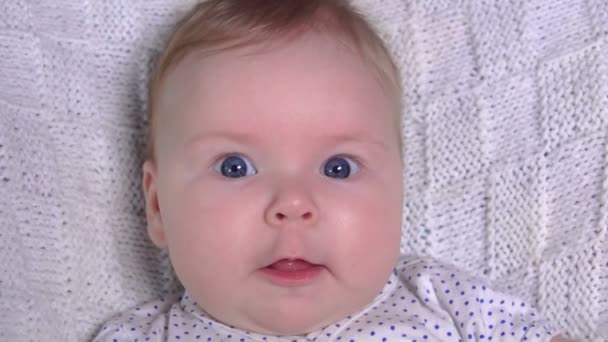 Mavi gözlü küçük bir bebeğin beyaz örgü ören battaniyesine yakın plan fotoğrafı. — Stok video