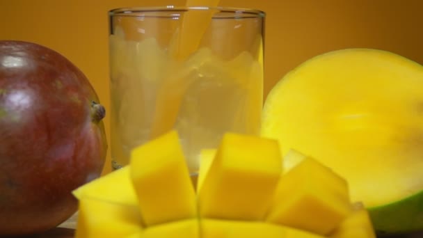 Φρέσκος χυμός μάνγκο χύνεται σε ένα ποτήρι δίπλα στο μεγάλο ώριμο μάνγκο κομμένο σε κύβους — Αρχείο Βίντεο