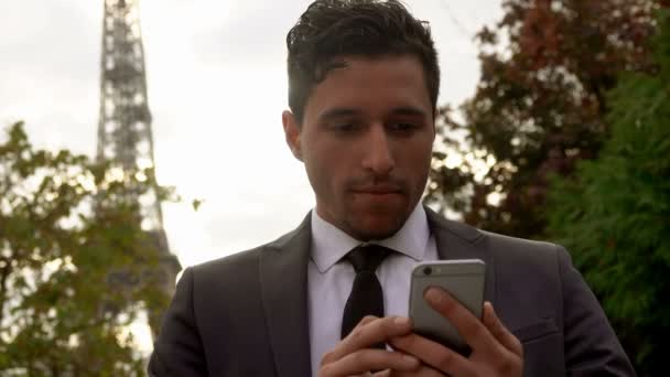 Бізнесмен дивиться на свій мобільний телефон на задньому плані Ейфелевої вежі. — стокове відео