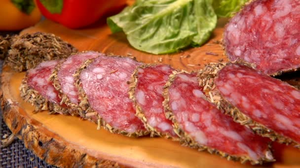 Вкусная сухая колбаса в травах вырезается на деревянной доске ножом — стоковое видео