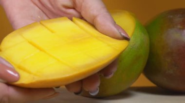 Dişi eller taze, olgun bir mangoyu açıyor. Küplere yarı yarıya bölünmüş.