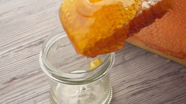 Fresh delicious honey flowing into the glass jar from the surface of honeycombs — Stock Video