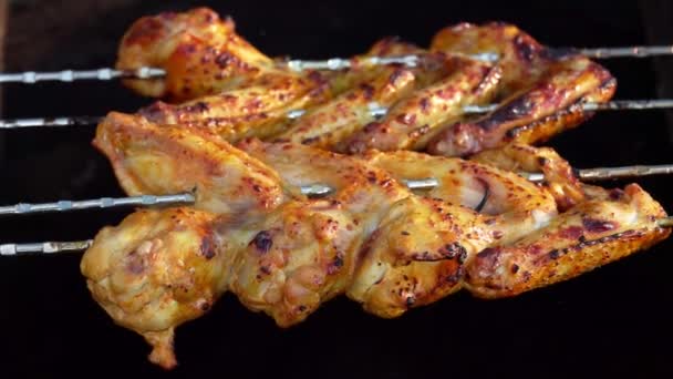 Las brochetas con las apetitosas alas de pollo están cambiando de lugar por encima del fuego abierto — Vídeos de Stock