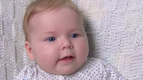 Un joli petit bébé aux yeux bleus sur une couverture tricotée blanche — Video