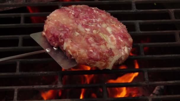Côtelette crue pour un hamburger est placé avec une spatule sur le gril au-dessus du feu — Video