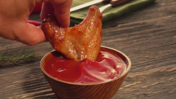 Großaufnahme einer männlichen Hand, die einen Hühnerflügel in Ketchup taucht — Stockvideo