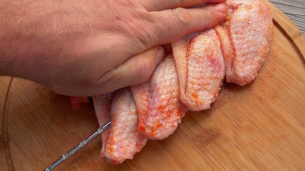 Ovanifrån av de manliga händerna genomträngande rå marinerad kyckling vingar med spett — Stockvideo