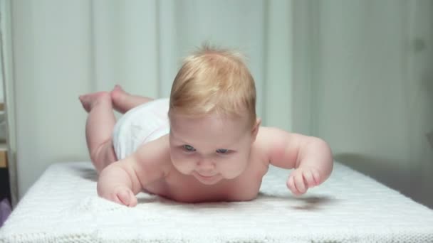 De kleine schattige baby ligt op de buik op een witte deken — Stockvideo