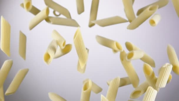 Penne de macarrão italiano seco voando para cima e girando em um fundo branco — Vídeo de Stock