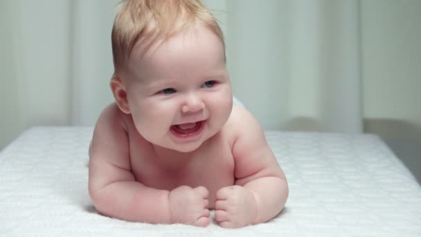 Pequeno bebê bonito está deitado no estômago em cobertor branco e rindo alegremente — Vídeo de Stock