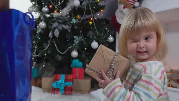 Kleines süßes Mädchen schaut neugierig in eine Papiertüte mit einem Weihnachtsgeschenk — Stockvideo