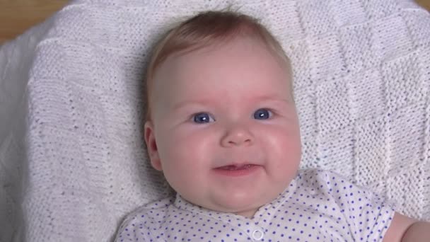 Pequeño lindo bebé de ojos azules en una manta blanca se ríe felizmente — Vídeos de Stock